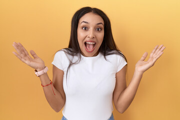 Young arab woman wearing casual white t shirt over yellow background celebrating crazy and amazed...