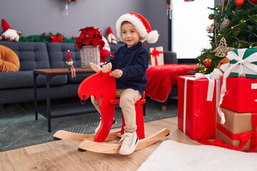 Adorable hispanic boy playing with reindeer rocking by christmas tree at home