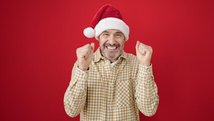 Middle age man smiling confident wearing christmas hat over isolated red background