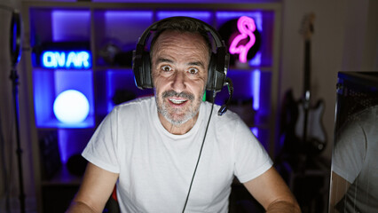 Smiling middle age man with grey hair commanding his stream! headphones on, gaming in his room till the wee hours! - obrazy, fototapety, plakaty