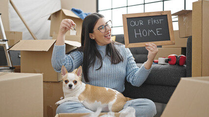 Young hispanic woman with chihuahua dog smiling confident holding blackboard and keys at new home