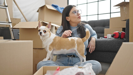 Young hispanic woman with chihuahua dog sitting thinking about an idea at new home