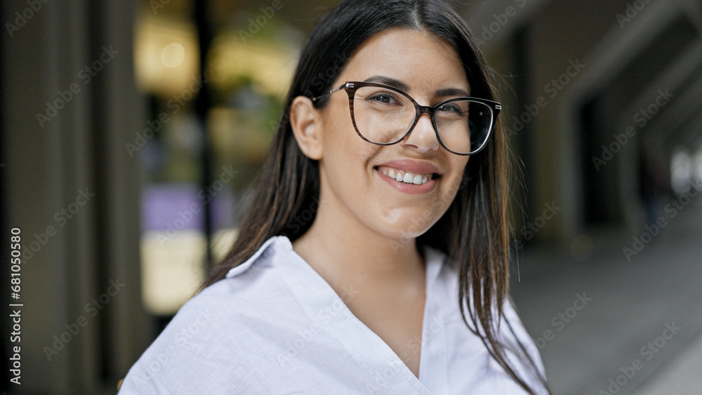 Sticker Young beautiful hispanic woman wearing glasses smiling happy in the streets of Madrid