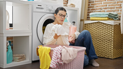 Obraz premium Young beautiful hispanic woman tired of doing laundry at laundry room