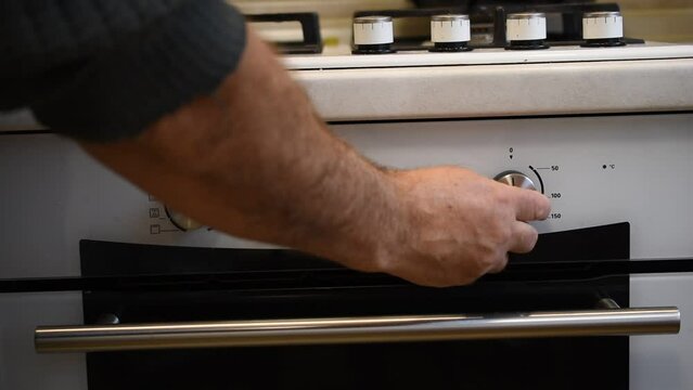 The man turns on the oven by turning the knobs located above the oven.
