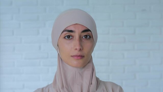 Portrait of self-sufficient Muslim woman in light hijab looking at camera. Close-up of young muslim woman standing against background of white brick wall. Concept Muslim women can be self-sufficient