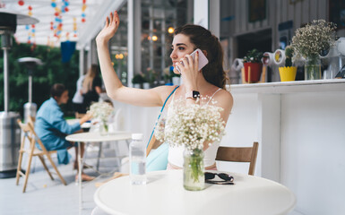 Active woman in sportswear hailing waiter while talking on mobile phone at outdoor cafe, multitasking in a vibrant urban setting
