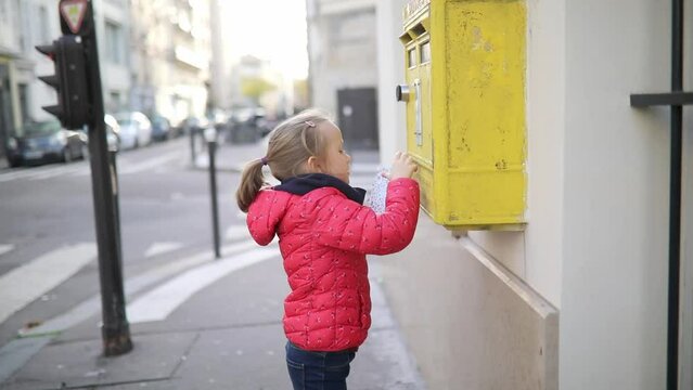 Adorable preschooler girl putting letter in yellow post box on a street of Paris