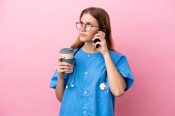 Young surgeon doctor woman isolated on pink background holding coffee to take away and a mobile