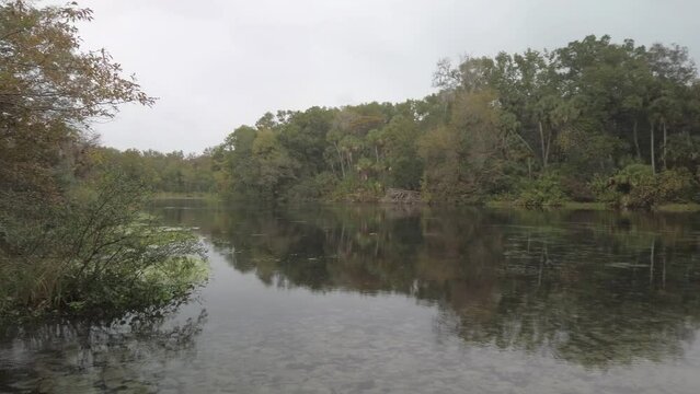 Pan left to right Silver Springs Florida Headspring view across water with trees on opposite side and reflections of clouds and trees in calm water.
