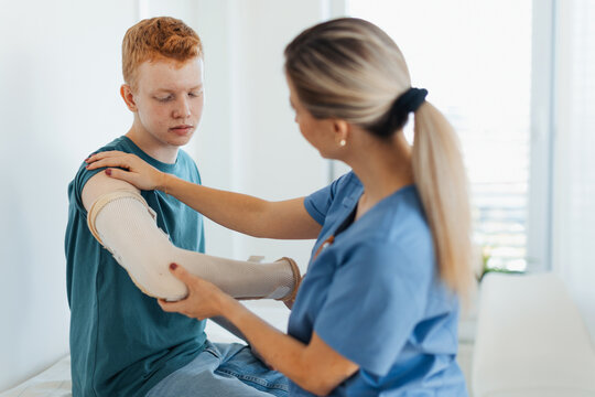 Doctor checking the orthopedic cast, brace on a teenage patient's broken arm. Teenage boy is healing a fracture after an accident.