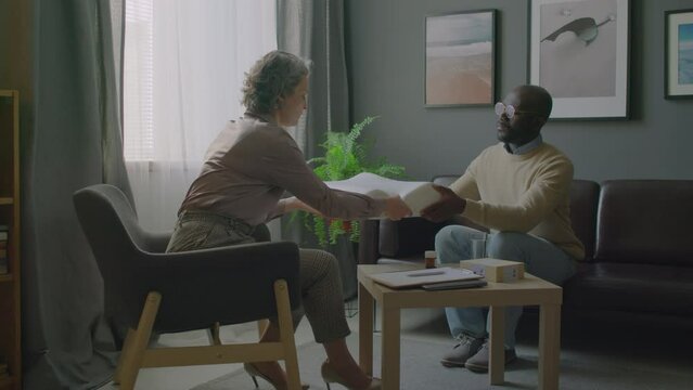 Zoom in shot of mature female somnologist giving orthopedic pillow and telling about sleep hygiene to African American patient during medical appointment in clinic