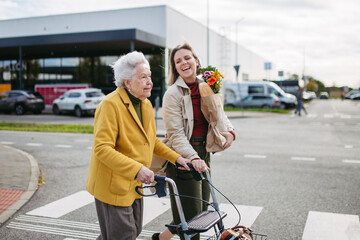 Mature granddaughter carrying grandmother's shopping bag. Senior woman and caregiver going to home...