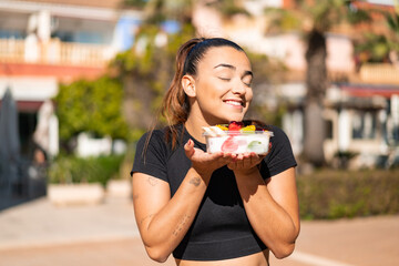 Young pretty brunette woman holding a bowl of fruit at outdoors