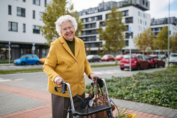 Senior woman with a mobility walker walking on city streets during autumn day, enjoying the beautiful sunny weather. Elderly lady savoring every moment, living life to fullest.