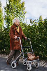 Senior woman with a mobility walker walking on city streets during autumn day, enjoying the...