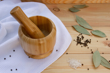 wooden mortar for grinding dried spices, pepper and others, next to pepper, salt, bay leaf, on a wooden table on a white cloth close-up