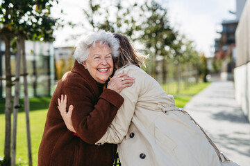 Grandmother and mature granddaughter on a walk in city park, during windy autumn day. Caregiver and...