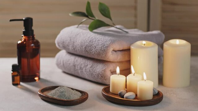 Beauty spa treatment items on white wooden table. Candles, stones, essential oils, mug, clay and towels. Cozy bath.