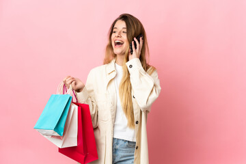 Fototapeta na wymiar Young woman with shopping bag isolated on pink background holding shopping bags and calling a friend with her cell phone