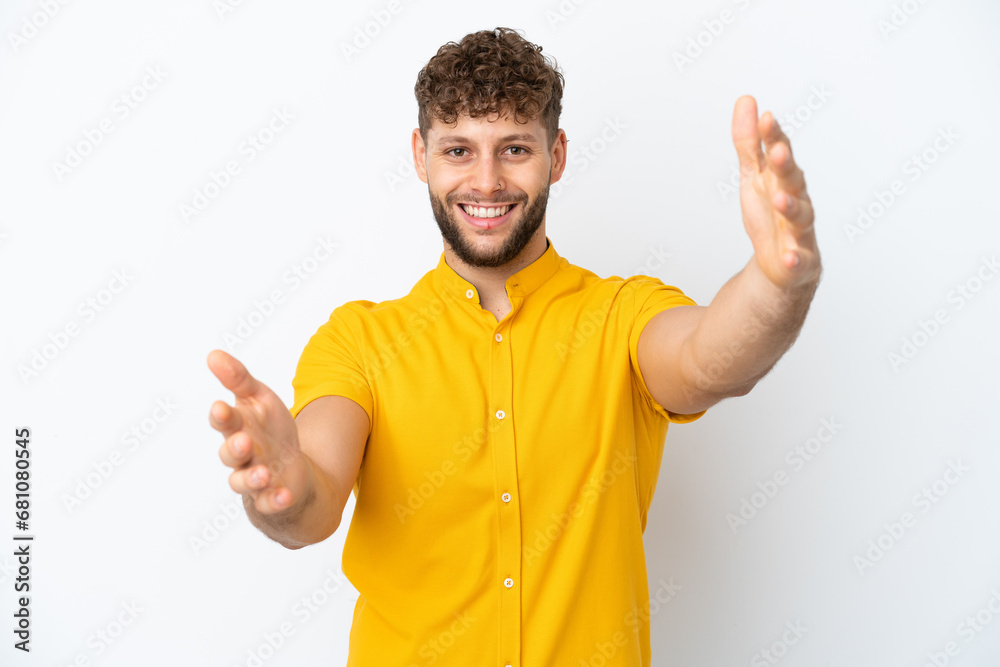 Wall mural Young handsome caucasian man isolated on white background presenting and inviting to come with hand