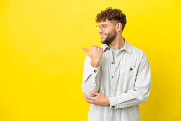 Young handsome caucasian man isolated on yellow background pointing to the side to present a product