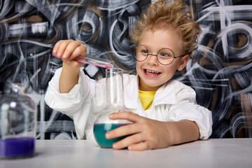 Child with a mad hairstyle rejoices, is engaged in his favorite scientific experiments. Young smart...
