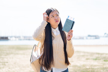 Young Chinese woman holding a passport at outdoors having doubts and with confuse face expression