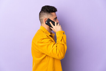 Fototapeta premium Caucasian man isolated on purple background keeping a conversation with the mobile phone with someone