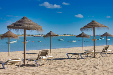 Straw umbrellas and sun loungers on the beach on a sunny day. The concept of rest and relaxation, holidays and travel. In the background the fishermen's boats.