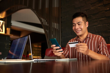 Smiling man uploading stock trading application and entering credit card information