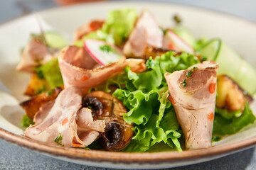 Macro shot in horizontal format, revealing the details of a salad with baked meat and fresh vegetables. Served on a ceramic plate, gray concrete background