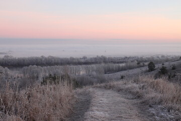 The light of the rising sun on the frost-covered trees, bushes and grass of the water meadows at the bend of the river