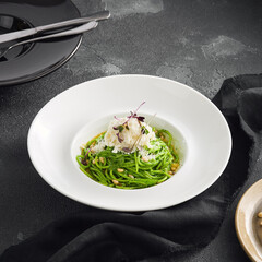 Elegantly plated pesto spaghetti with creamy stracciatella cheese and toasted pine nuts, served in a white bowl on a sleek black surface