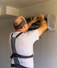 Air conditioning technician; Air conditioning technician repairing a split air conditioner in the living room of a small apartment