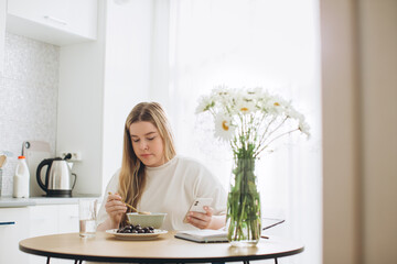 The blonde girl has breakfast while holding the phone in her hands.