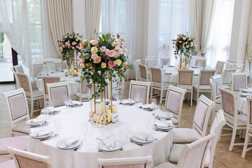 Wedding decorations. Served wedding table with decorative fresh white and pink flowers, candles. Celebration details. Flower composition roses, plates, candles in candlesticks 