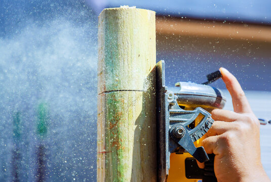An electric saw is being used by worker to cut wooden post for fence
