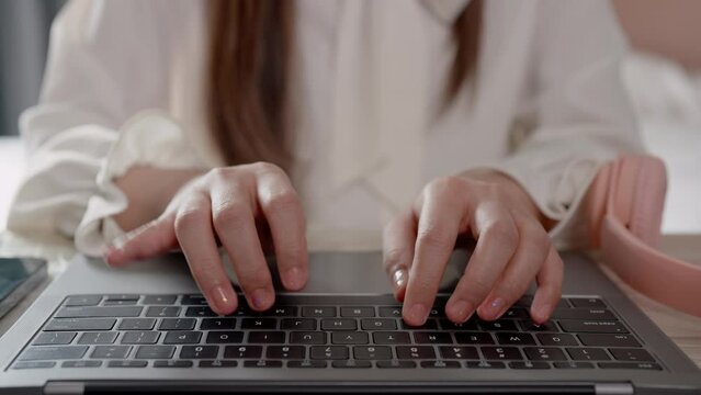 Close-up of Asian woman's fingers pressing keyboard on laptop computer Sitting at home, working on the bed, typing documents with speed and accuracy in the bedroom.