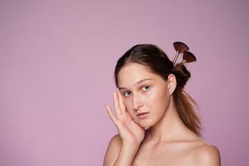 Naklejka premium Portrait of young seminude woman in studio on pink background in pink neon light close up. Womans hair is pinned up with makeup brushes. Beauty, cosmetology, care.