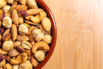 Roasted, peeled, salted peanuts, hazelnuts, cashews, almonds, pistachios. Free text space on wooden background. Close-up top view mixed nuts in bowl in selective focus on wooden background.