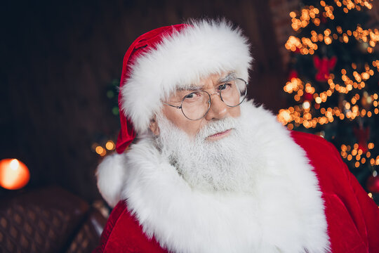 Photo of cool confident santa claus wear red costume spectacles looking you indoors new year north pole office - Powered by Adobe