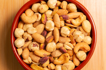 Roasted, peeled, salted peanuts, hazelnuts, cashews, almonds, pistachios. Mixed nuts in bowl on wooden background, top view.