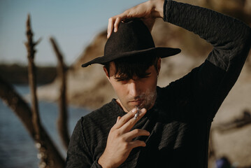 Handsome young man in a wide-brimmed hat smokes on the beach