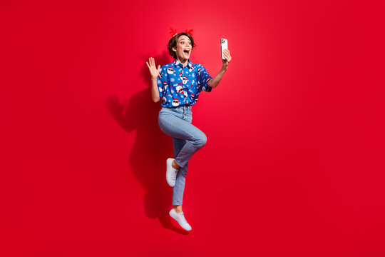 Full body photo jump girl of waving palm phone video greeting follower happy new year festive atmosphere isolated on red color background