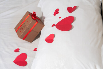 Valentine gift on bed with white bedding and red love.