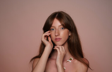 Portrait of seminude woman in studio on brown background close up. A multitude of white wildflowers are taped to the woman's chest with duct tape. Female beauty, health and body care.