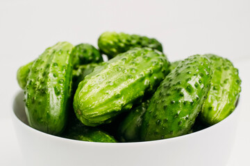 Green cucumbers in a white plate on a white background.