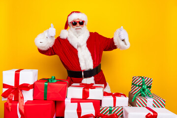 Photo of elderly cheerful santa demonstrate thumb up approval pile stack new year giftbox isolated on yellow color background