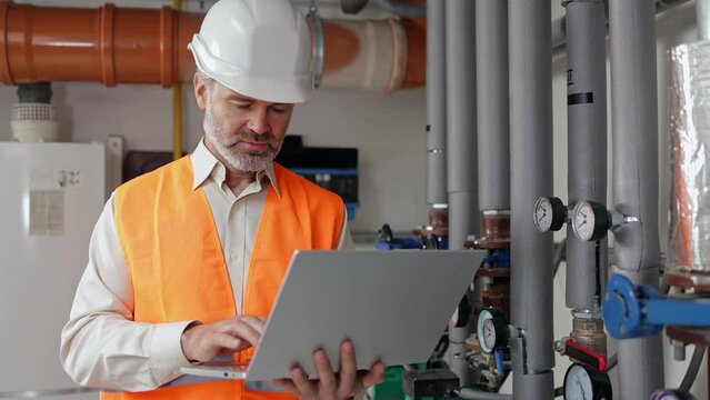 Petrochemical worker supervise the operation of gas and oil pipelines in the factory. Caucasian worker in protective suit using laptop while checking machines in heating plant